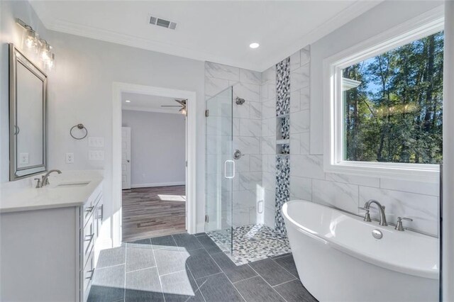 bathroom with plus walk in shower, hardwood / wood-style floors, crown molding, ceiling fan, and vanity