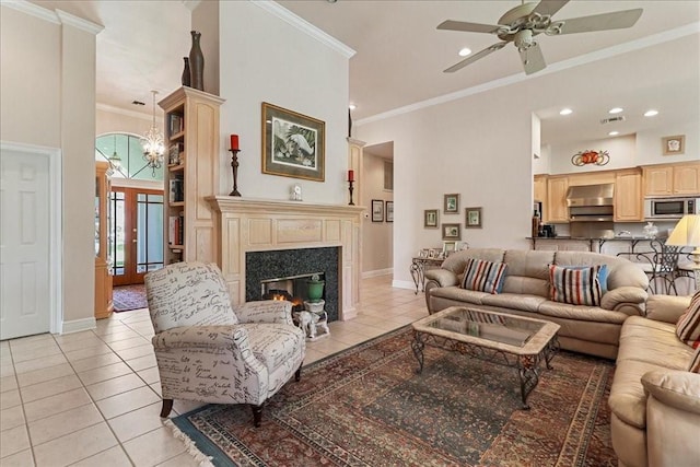 living room with ceiling fan with notable chandelier, a high end fireplace, light tile patterned floors, a high ceiling, and ornamental molding