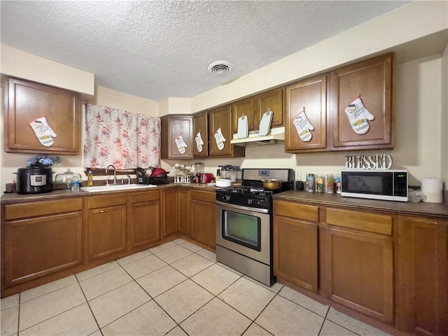 4651 Lancelot Dr, New Orleans, LA 70127 - kitchen with gas stove, white microwave, dark countertops, a sink, and under cabinet range hood