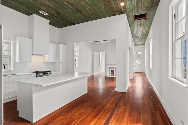 kitchen with white cabinetry, a fireplace, stainless steel range with gas cooktop, ceiling fan, and dark hardwood / wood-style floors