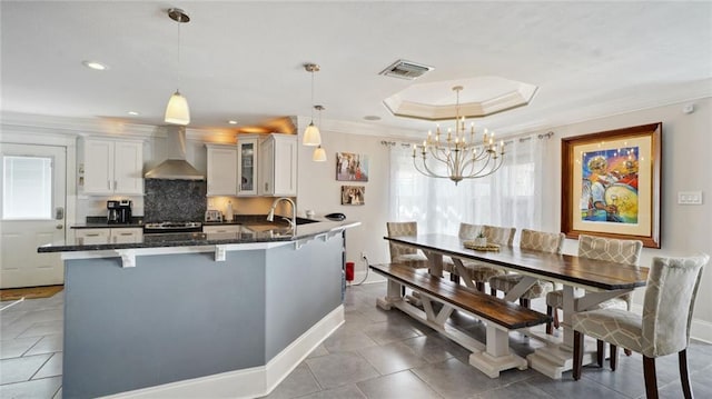 kitchen featuring wall chimney range hood, a kitchen breakfast bar, white cabinetry, stainless steel stove, and decorative light fixtures