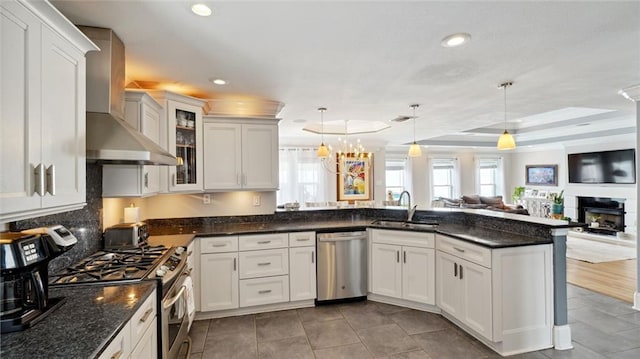 kitchen with a wealth of natural light, hanging light fixtures, stainless steel appliances, and wall chimney exhaust hood