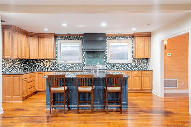 kitchen with a breakfast bar area, light hardwood / wood-style flooring, a center island, and range hood