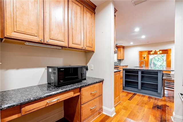 kitchen featuring light wood-type flooring, dark stone countertops, and sink