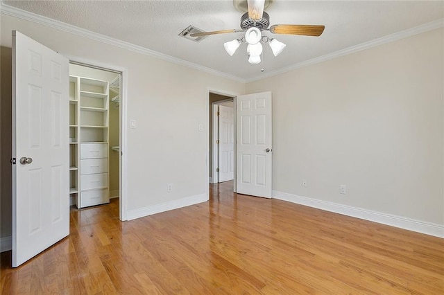 unfurnished bedroom with a walk in closet, crown molding, ceiling fan, light wood-type flooring, and a closet