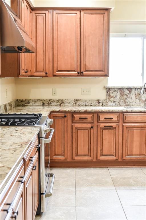 kitchen with light stone counters, sink, light tile patterned floors, ventilation hood, and stainless steel gas range oven