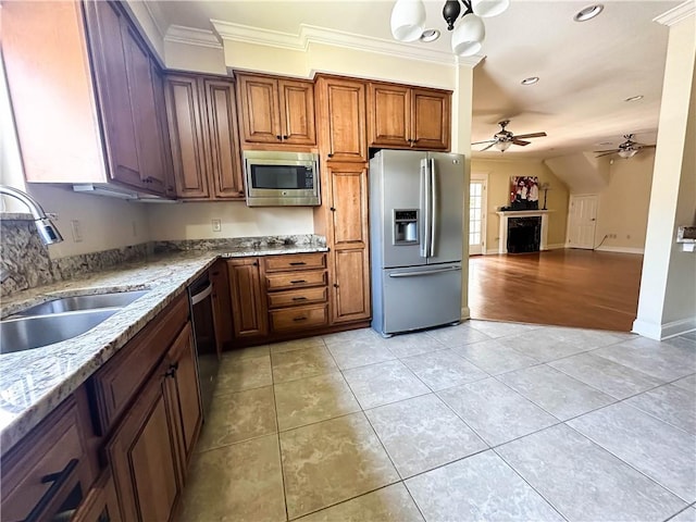 kitchen with light stone counters, ceiling fan with notable chandelier, stainless steel appliances, crown molding, and sink