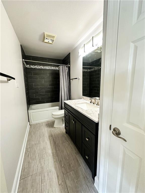 6613 Memphis St, New Orleans, LA 70124 - bathroom featuring wood finished floors, toilet, vanity, and shower / bathtub combination with curtain