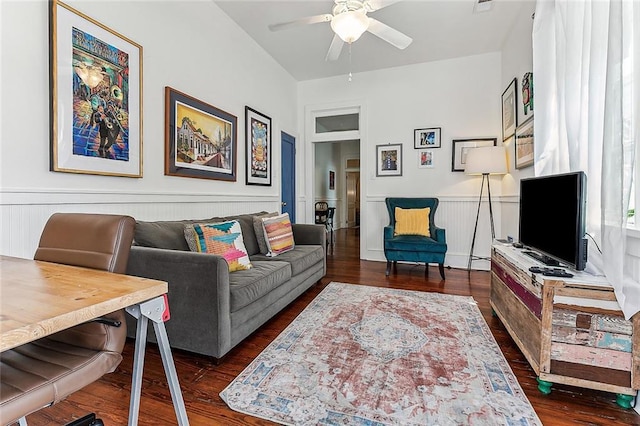 living room with a wainscoted wall, dark wood-type flooring, and a ceiling fan