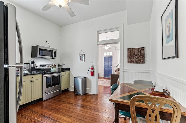 kitchen featuring a ceiling fan, dark countertops, stainless steel appliances, cream cabinetry, and wainscoting
