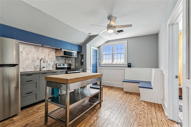 kitchen with light wood-type flooring, sink, appliances with stainless steel finishes, blue cabinets, and ceiling fan