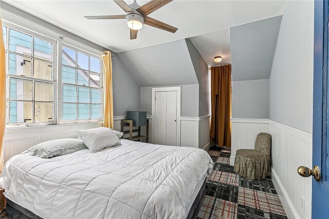 bedroom featuring a wainscoted wall, lofted ceiling, and ceiling fan