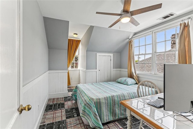 bedroom with ceiling fan, lofted ceiling, a wainscoted wall, and visible vents