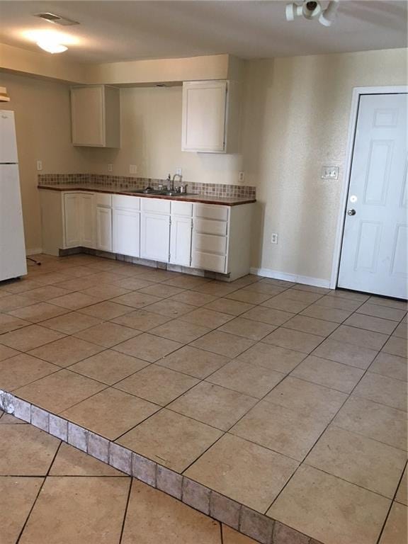 kitchen featuring white cabinets, light tile patterned floors, white fridge, and sink