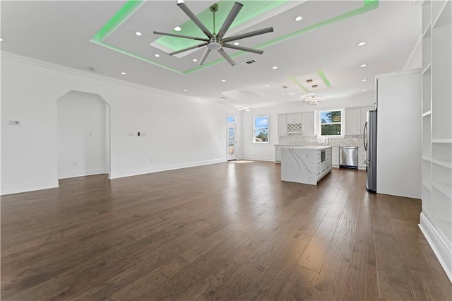 unfurnished living room featuring ceiling fan, a raised ceiling, sink, dark wood-type flooring, and crown molding