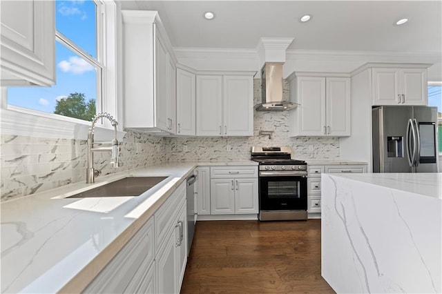 kitchen with light stone counters, white cabinets, appliances with stainless steel finishes, and wall chimney range hood