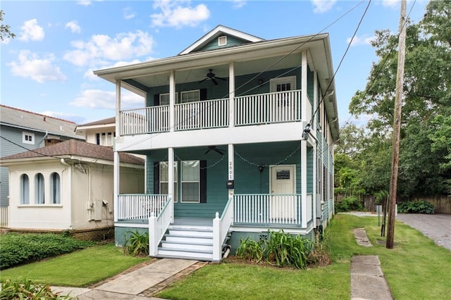 view of front facade with a balcony, a porch, ceiling fan, and a front yard