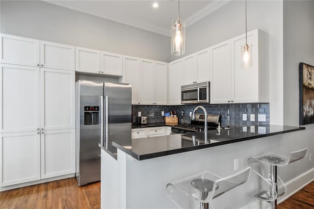 kitchen with pendant lighting, hardwood / wood-style flooring, white cabinetry, kitchen peninsula, and appliances with stainless steel finishes