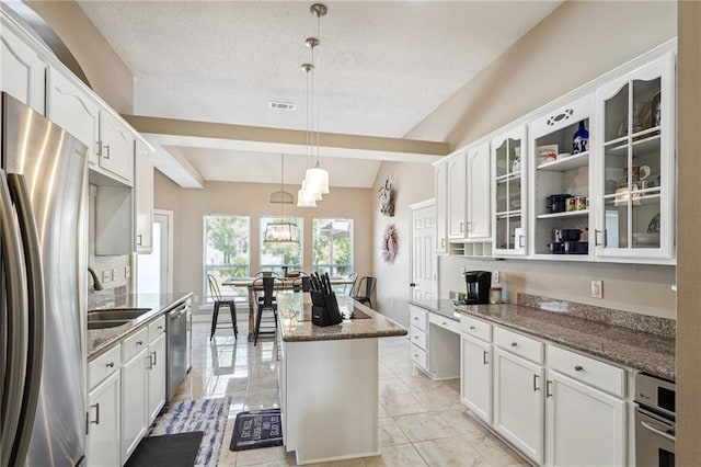 kitchen featuring a center island, white cabinets, hanging light fixtures, stainless steel appliances, and dark stone countertops