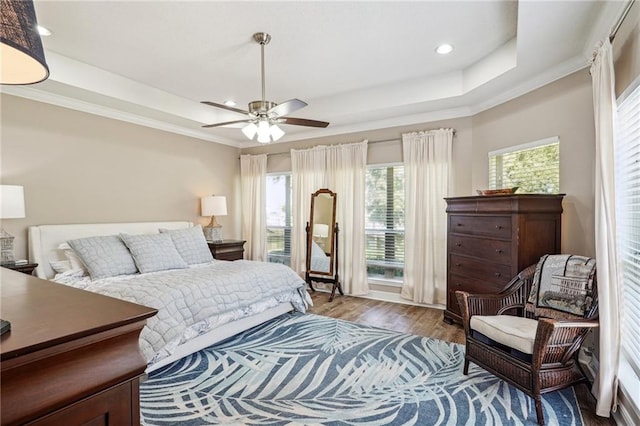 bedroom with wood-type flooring, a tray ceiling, ceiling fan, and ornamental molding