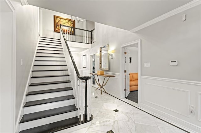 stairs featuring marble finish floor, ornamental molding, a decorative wall, and wainscoting