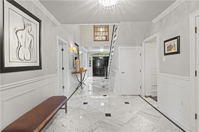 entrance foyer with an inviting chandelier, ornamental molding, marble finish floor, and a decorative wall