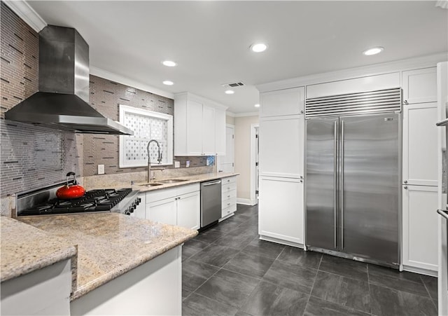 kitchen featuring tasteful backsplash, light stone countertops, stainless steel appliances, wall chimney range hood, and a sink