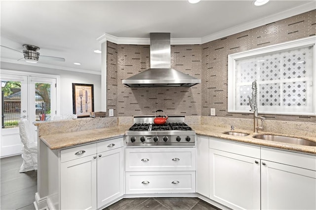 kitchen with wall chimney exhaust hood, ornamental molding, backsplash, stovetop, and a sink