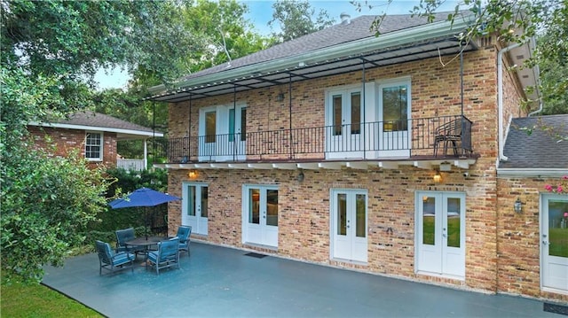 back of property featuring a patio, a balcony, brick siding, french doors, and roof with shingles