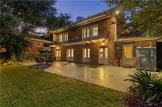 back of property at dusk featuring french doors, brick siding, a yard, a patio area, and a balcony