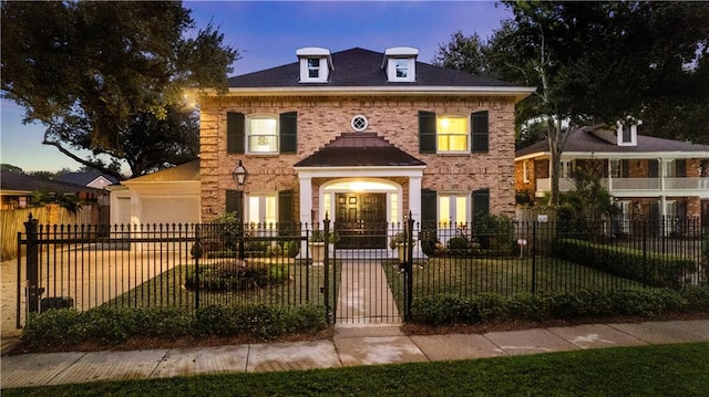 colonial house featuring a fenced front yard, brick siding, and a garage