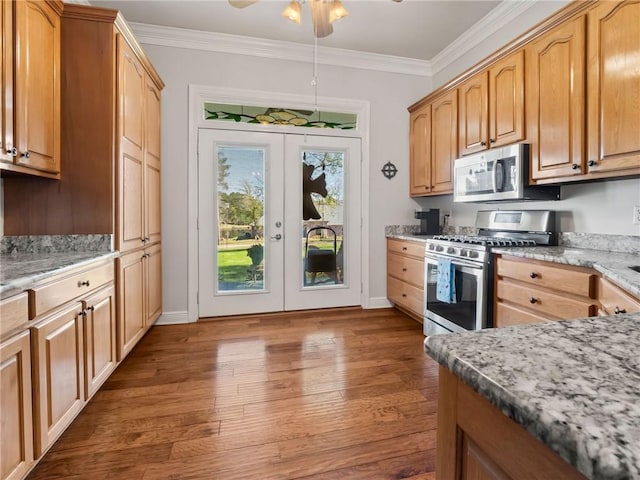 kitchen featuring appliances with stainless steel finishes, dark wood-type flooring, light stone counters, ceiling fan, and ornamental molding