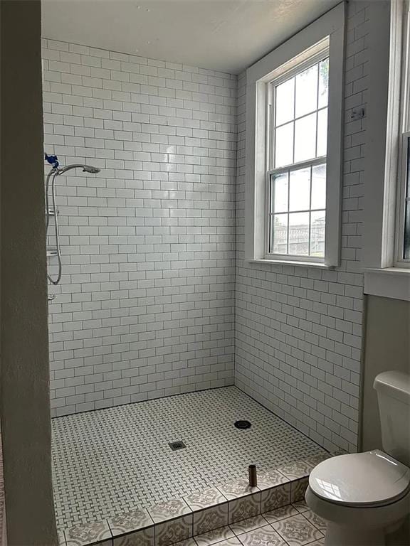 bathroom featuring tile patterned flooring, toilet, and a tile shower