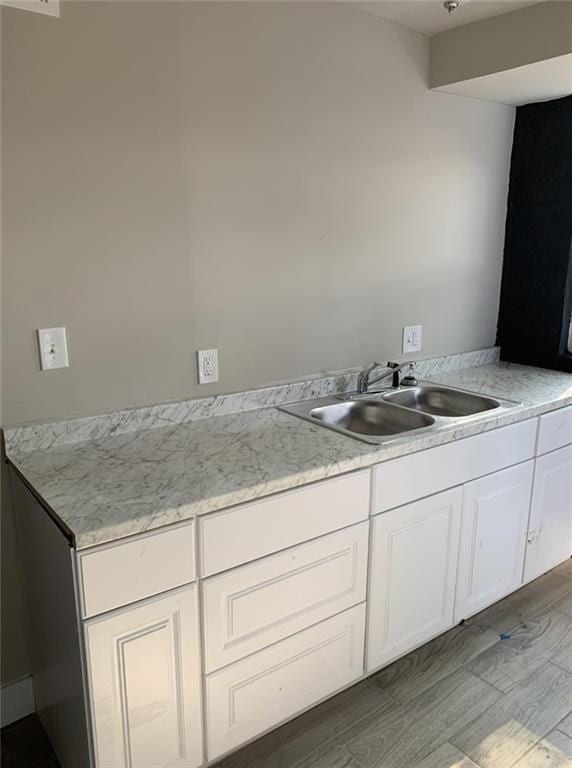 kitchen with wood-type flooring, light stone counters, white cabinetry, and sink