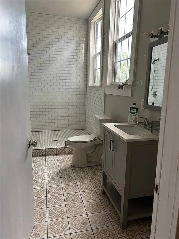 bathroom featuring tile patterned flooring, a tile shower, vanity, and toilet