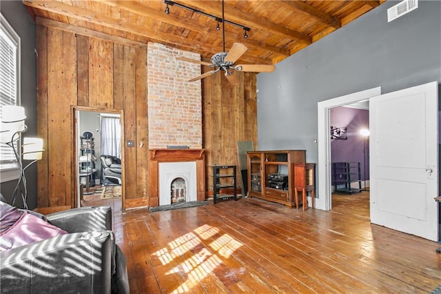 unfurnished living room with wood ceiling, beamed ceiling, a large fireplace, ceiling fan, and hardwood / wood-style floors