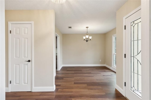 unfurnished dining area featuring an inviting chandelier, a textured ceiling, and dark hardwood / wood-style floors