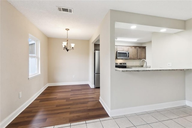 kitchen with kitchen peninsula, wood-type flooring, appliances with stainless steel finishes, a notable chandelier, and light stone countertops