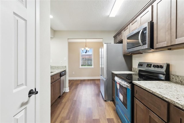 kitchen featuring a textured ceiling, appliances with stainless steel finishes, an inviting chandelier, light stone countertops, and light hardwood / wood-style floors