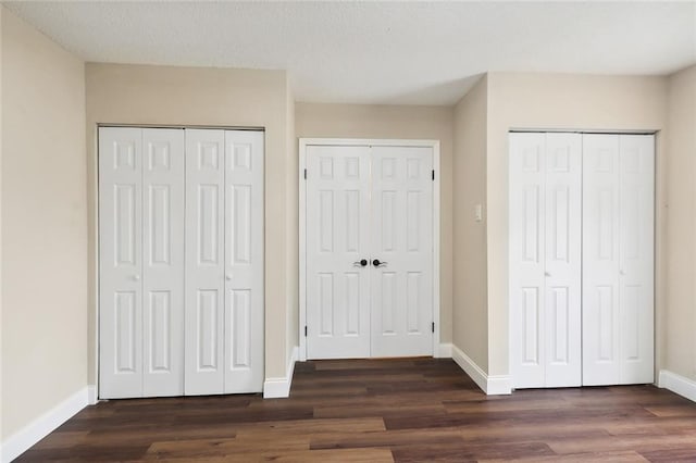 unfurnished bedroom with multiple closets and dark wood-type flooring