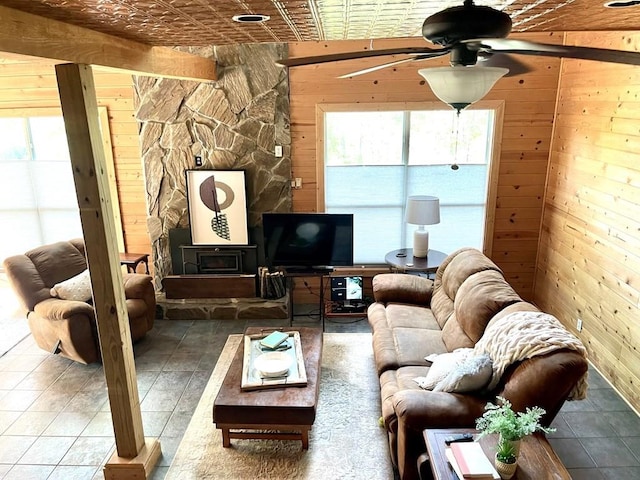 living room with ceiling fan, wooden walls, and a wood stove