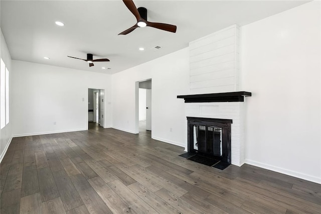 unfurnished living room featuring dark hardwood / wood-style floors, a large fireplace, and ceiling fan