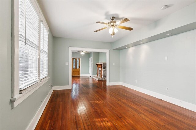 spare room with a brick fireplace, ceiling fan, and dark hardwood / wood-style floors