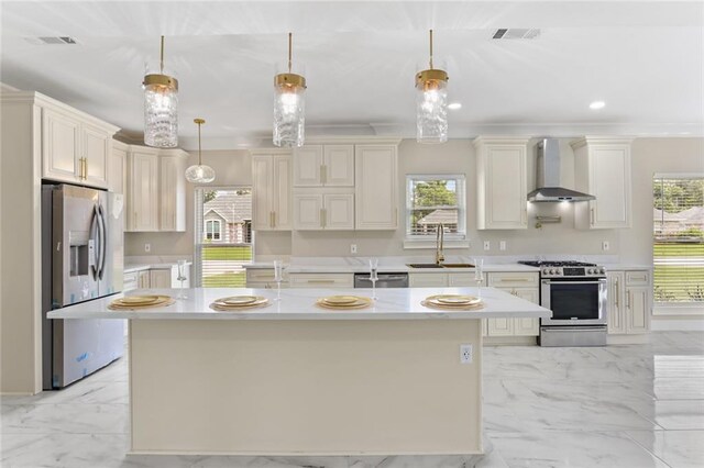 kitchen featuring pendant lighting, an island with sink, wall chimney exhaust hood, appliances with stainless steel finishes, and a healthy amount of sunlight