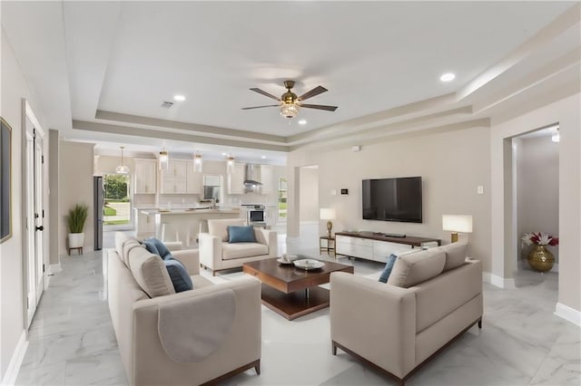 living room with ceiling fan and a raised ceiling