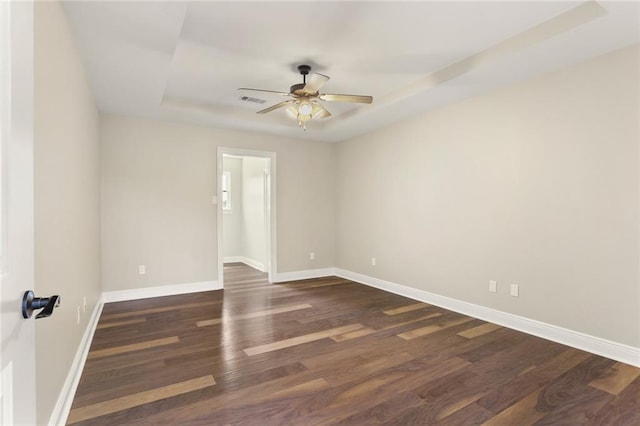 spare room with a tray ceiling, ceiling fan, and dark hardwood / wood-style flooring