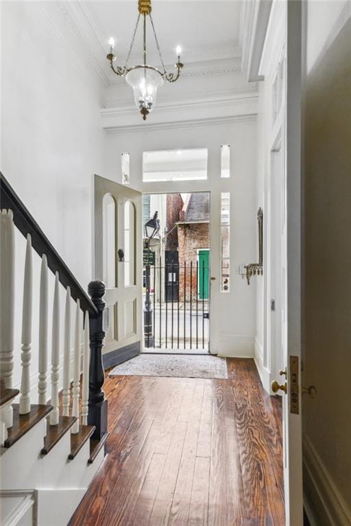 foyer entrance with wood-type flooring, an inviting chandelier, and crown molding