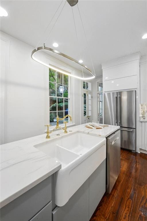 kitchen with dark wood-type flooring, sink, white cabinets, appliances with stainless steel finishes, and light stone countertops