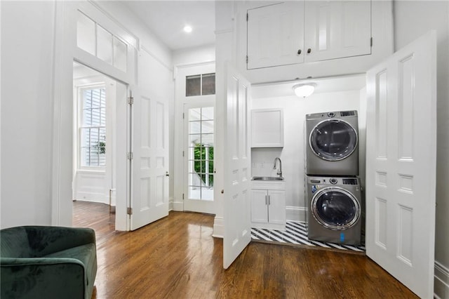 clothes washing area featuring stacked washer / dryer, dark hardwood / wood-style flooring, sink, and cabinets