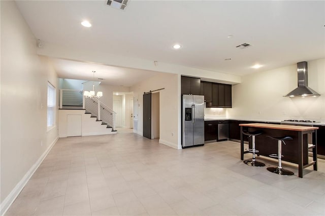 kitchen with a breakfast bar area, wall chimney range hood, a barn door, an inviting chandelier, and appliances with stainless steel finishes